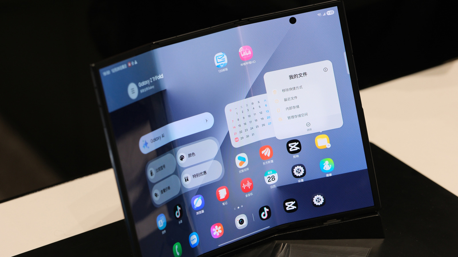 A foldable phone opened on a table displays a home screen with app icons and widgets.