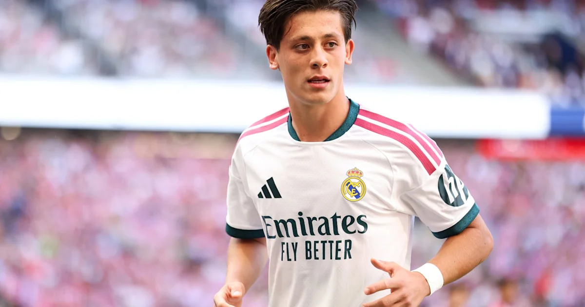 A young footballer in a white Real Madrid shirt runs on the pitch during a match.