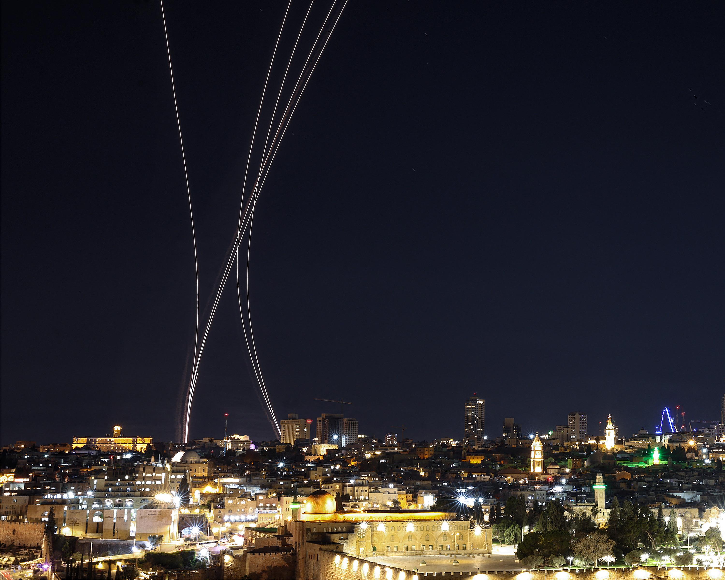 Night view of a city skyline beneath several bright, curved trails rising into the sky.