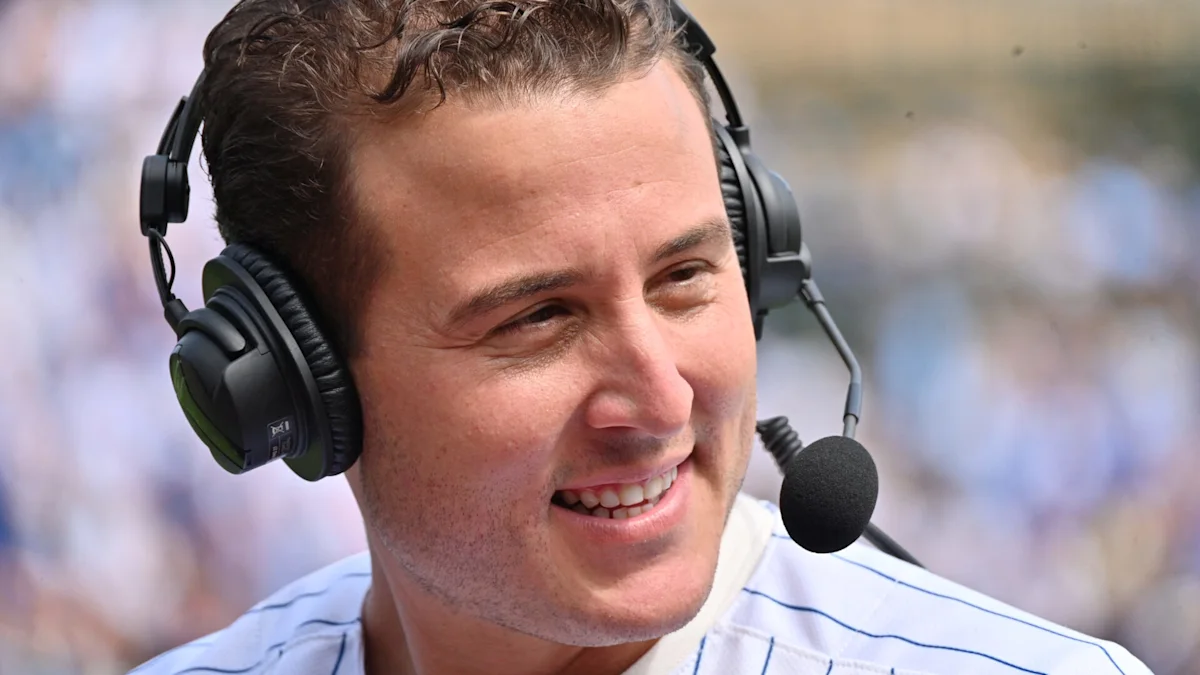 A smiling man in a pinstriped shirt wears a headset with a microphone.