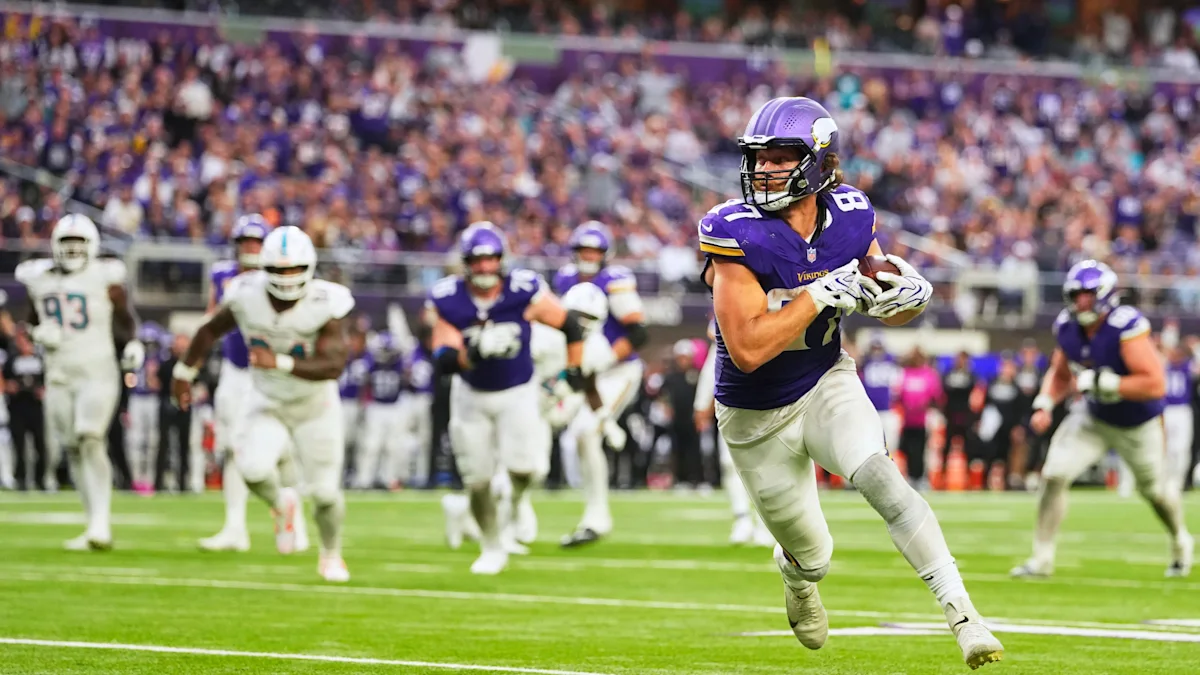 A Vikings player in purple carries the football as defenders pursue across the field.