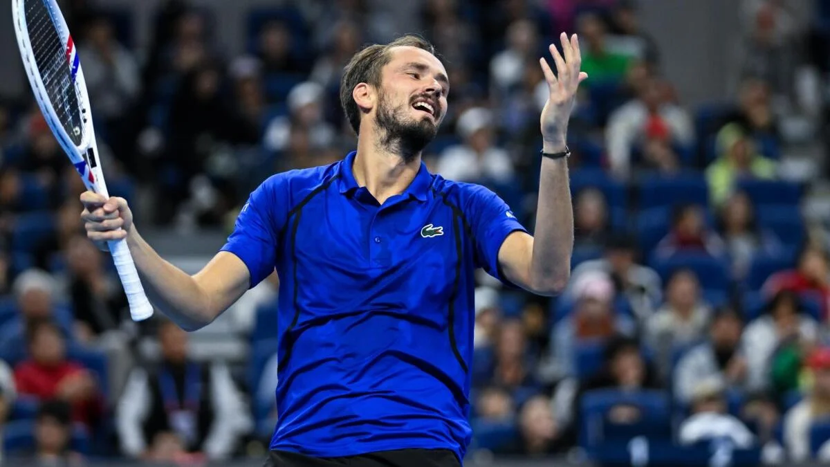 Tennis player in a blue shirt holds his racket and raises one hand during a match.