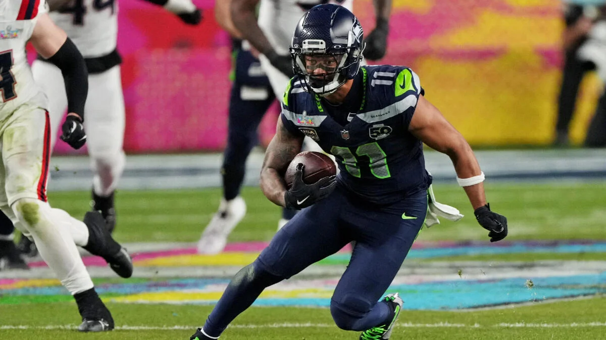 Seattle Seahawks player in navy uniform runs with the football as opponents pursue him.