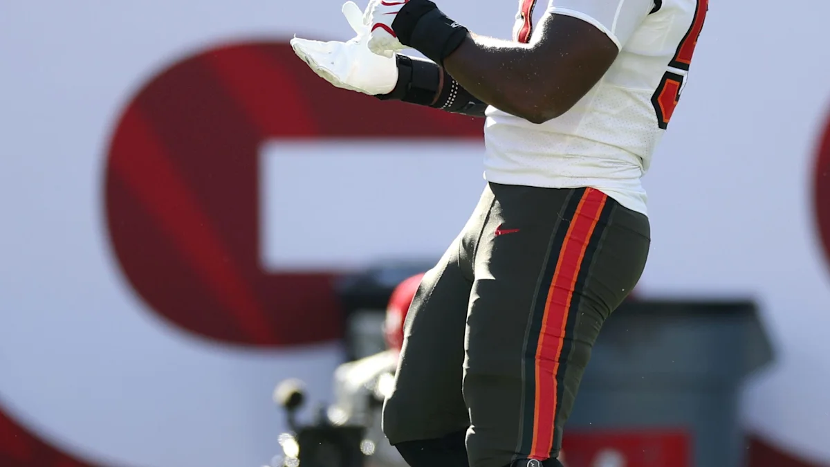 Cropped view of a football player in a white jersey and dark pants with red and orange stripes.