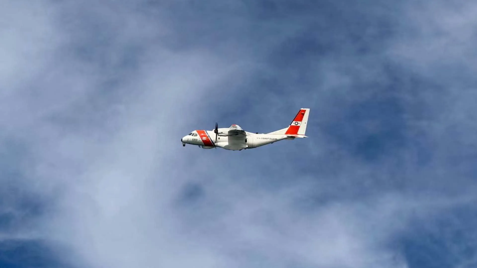White and red turboprop aircraft flying through a cloudy blue sky.
