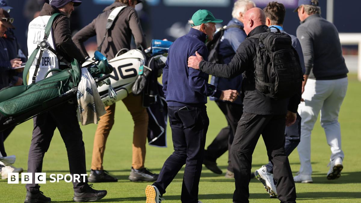 Several men gather on a golf course, with one placing a hand on another’s shoulder beside golf bags.