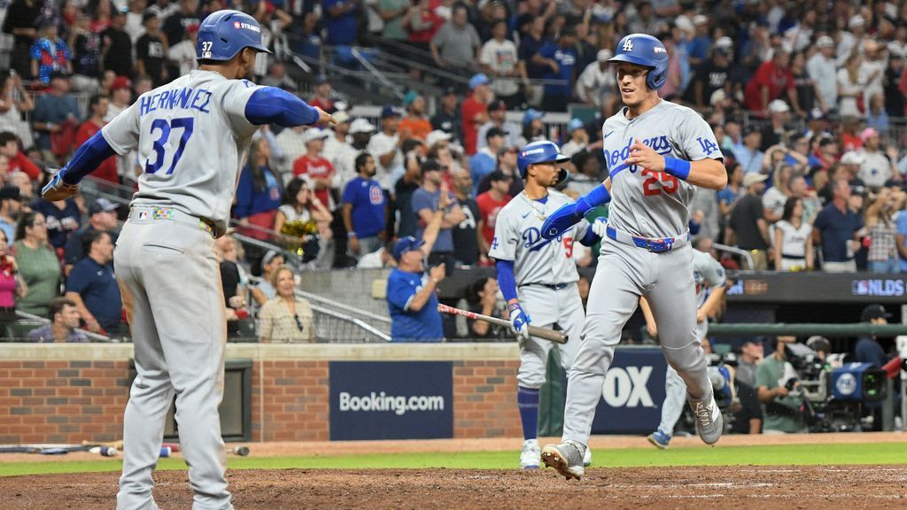 Two Dodgers players meet on the field as a teammate jogs toward them after a play.
