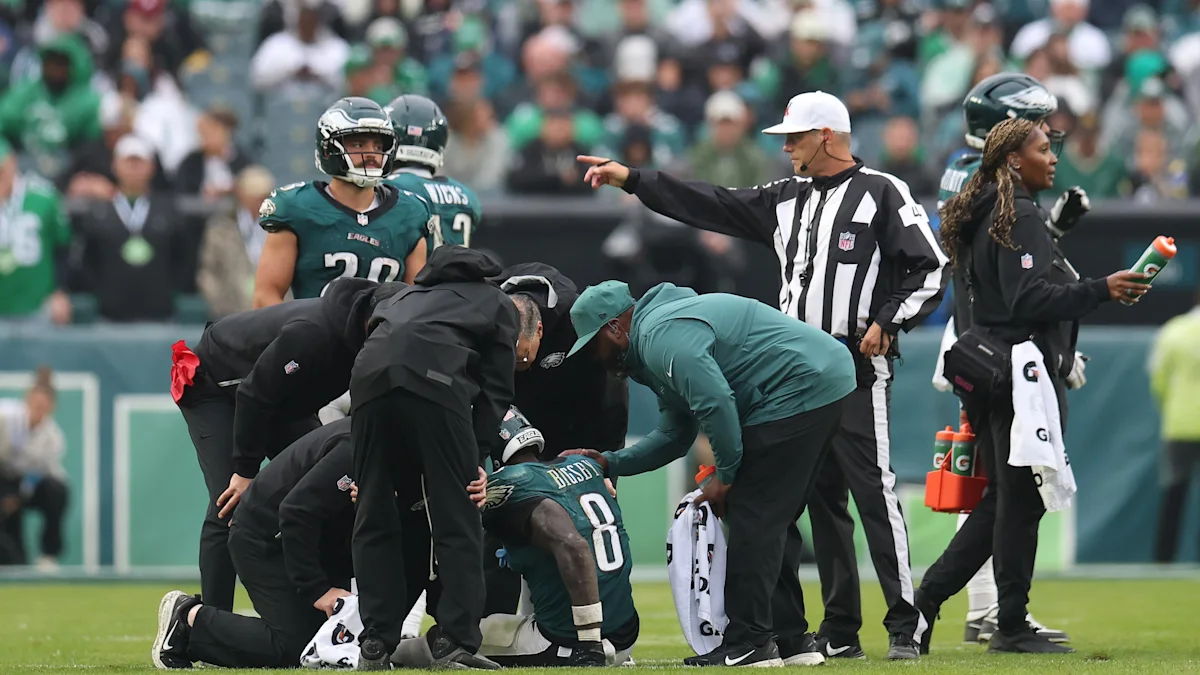 Eagles players and staff gather around an injured teammate on the field as an official points nearby.