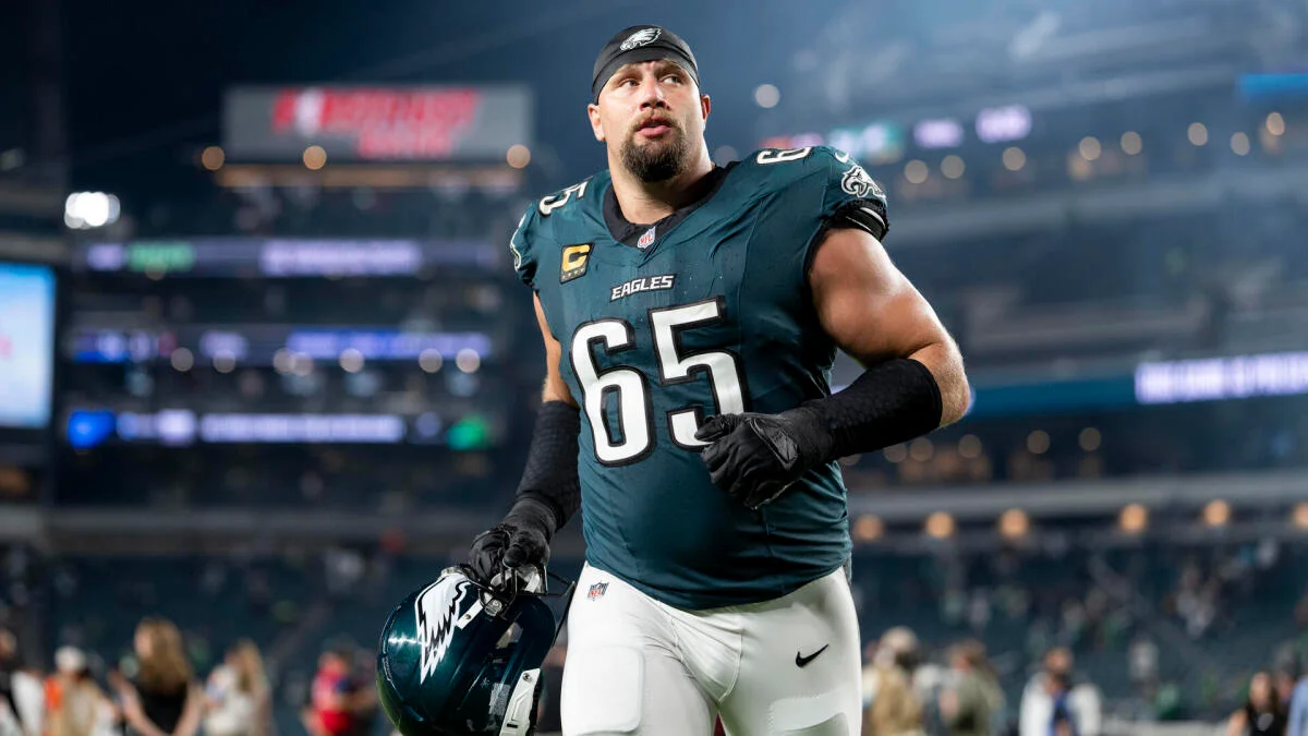 Philadelphia Eagles player in a number 65 jersey holds his helmet on the field.