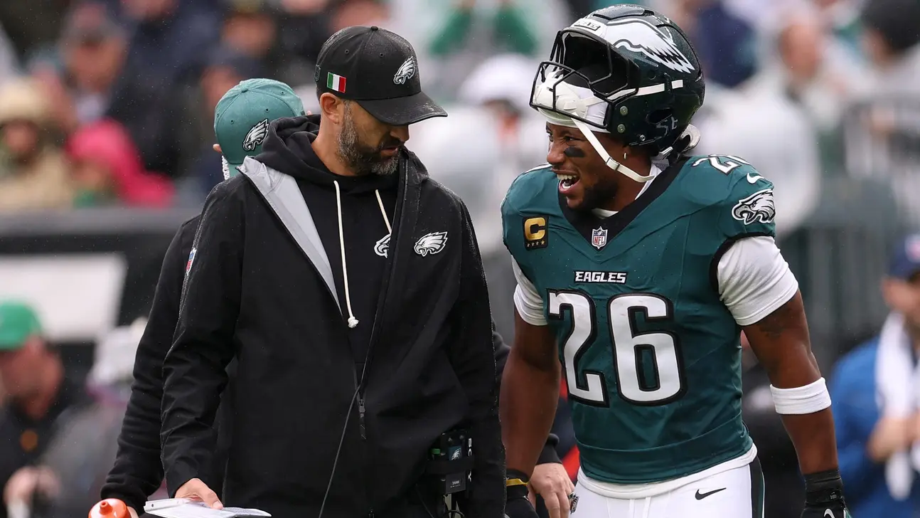 Eagles player in a teal number 26 jersey talks with a coach on the sideline.