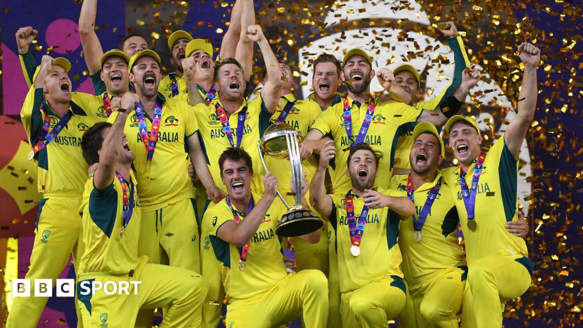 Australian cricket players celebrate with a trophy and medals as gold confetti falls around them.