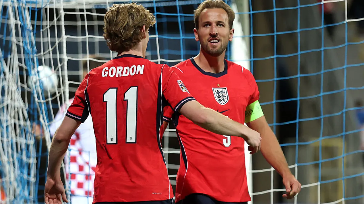 Two England players in red shirts celebrate in front of the goal net, one wearing a captain's armband.