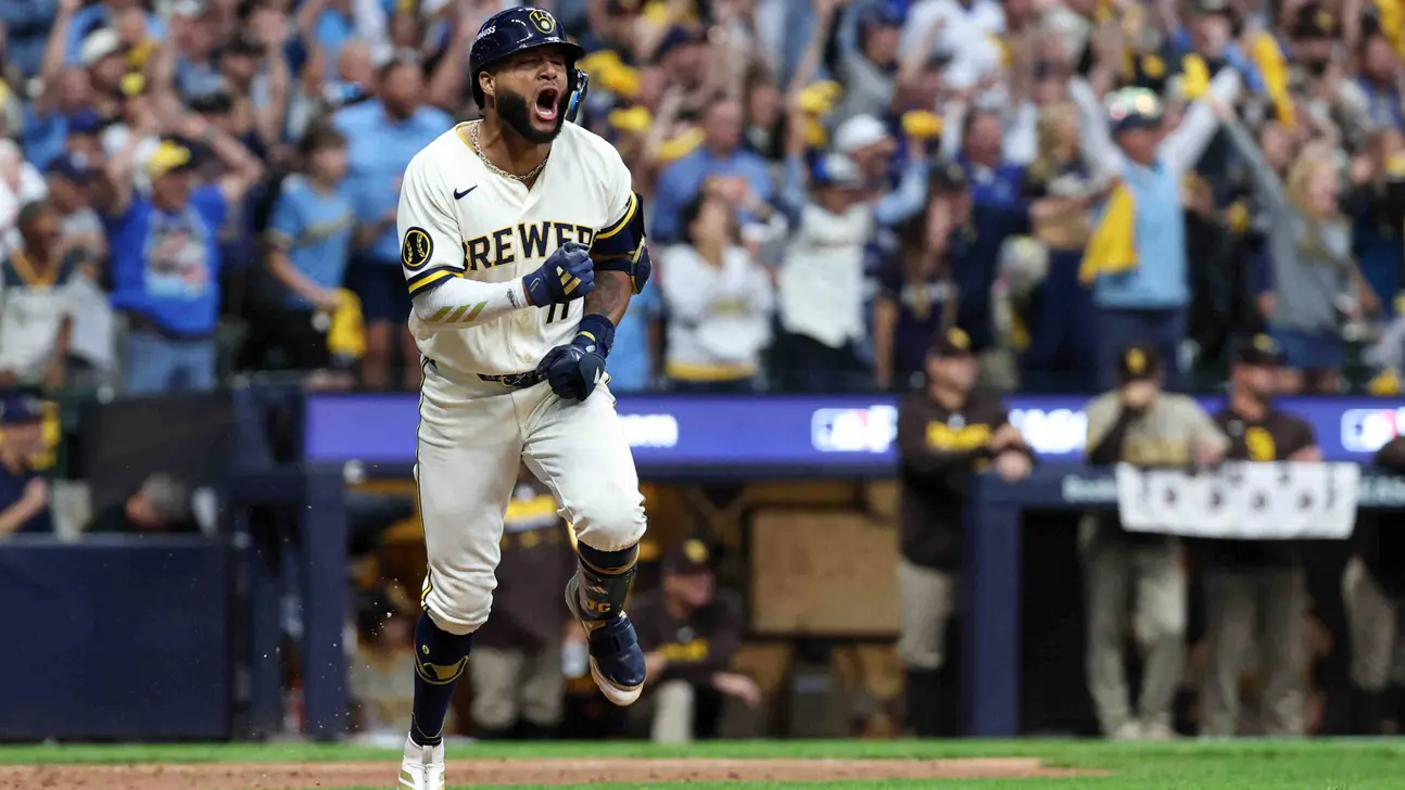 Brewers player in a white uniform celebrates while running across the field before a cheering crowd.