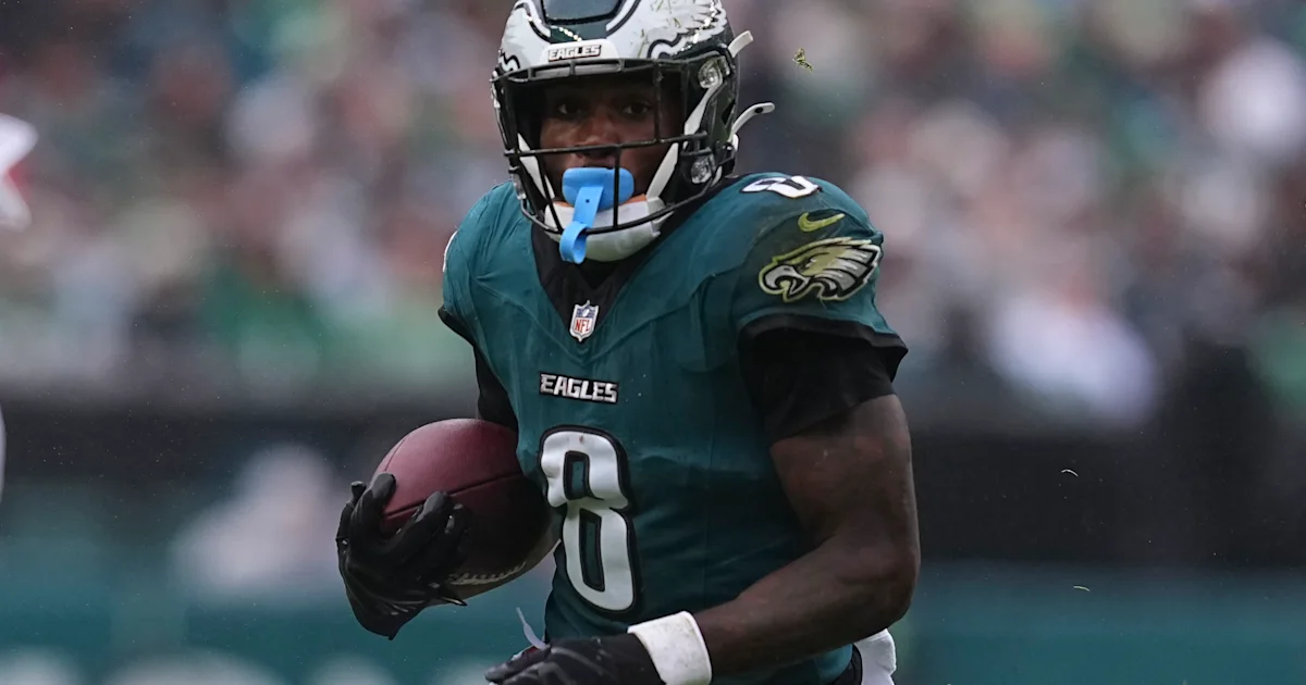 An Eagles player in a dark green number 0 jersey carries a football during a game.