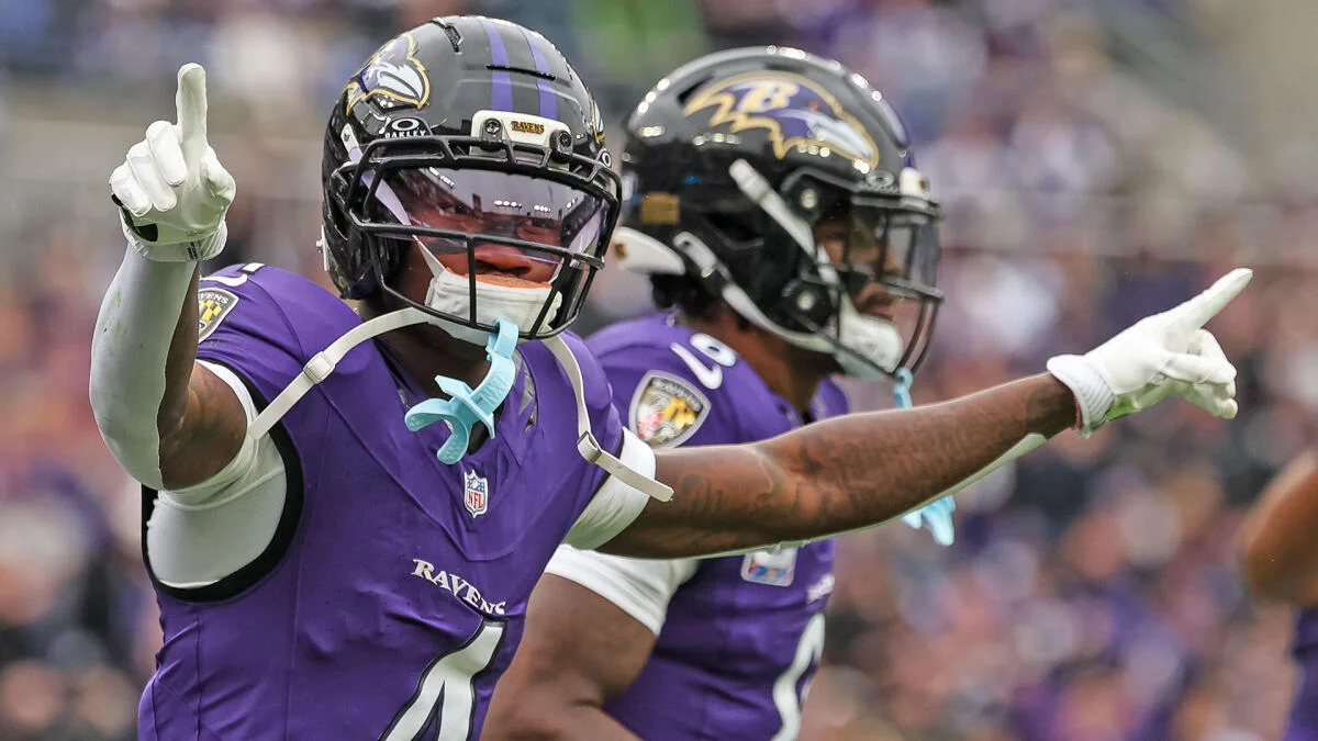 Two Baltimore Ravens players in purple uniforms celebrate with arms extended on the field.