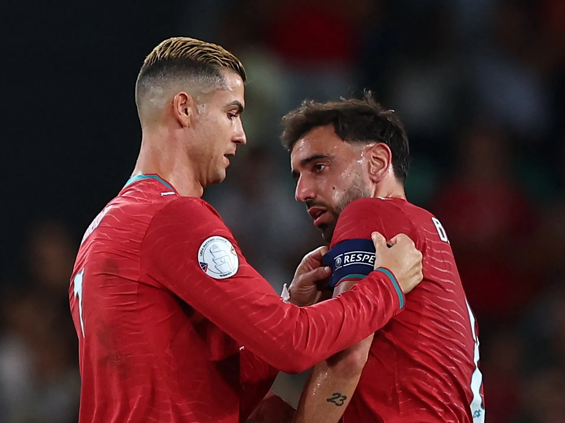 Two Portugal players in red kits speak closely as one places his hands on the other's shoulders.