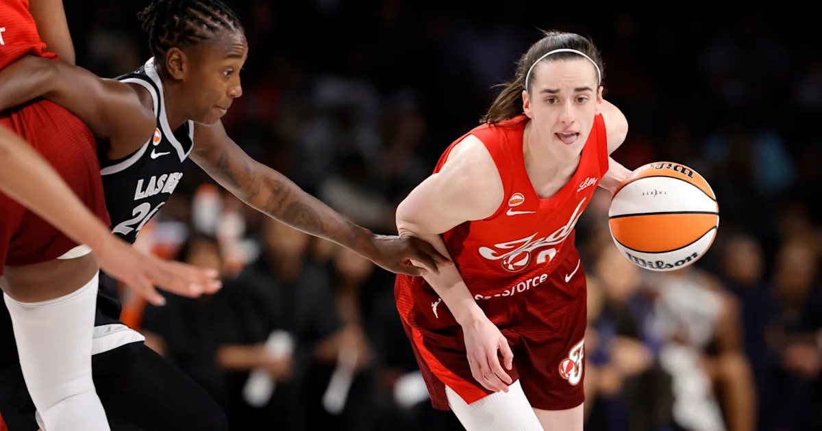 A player in a red uniform dribbles past a defender in a black uniform during a basketball game.