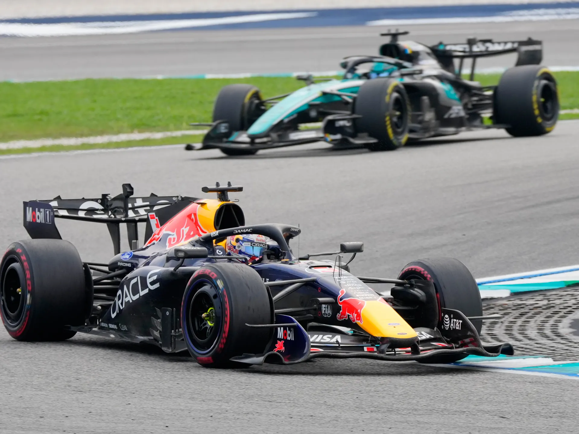 A Red Bull Formula One car leads a Mercedes car through a circuit corner.