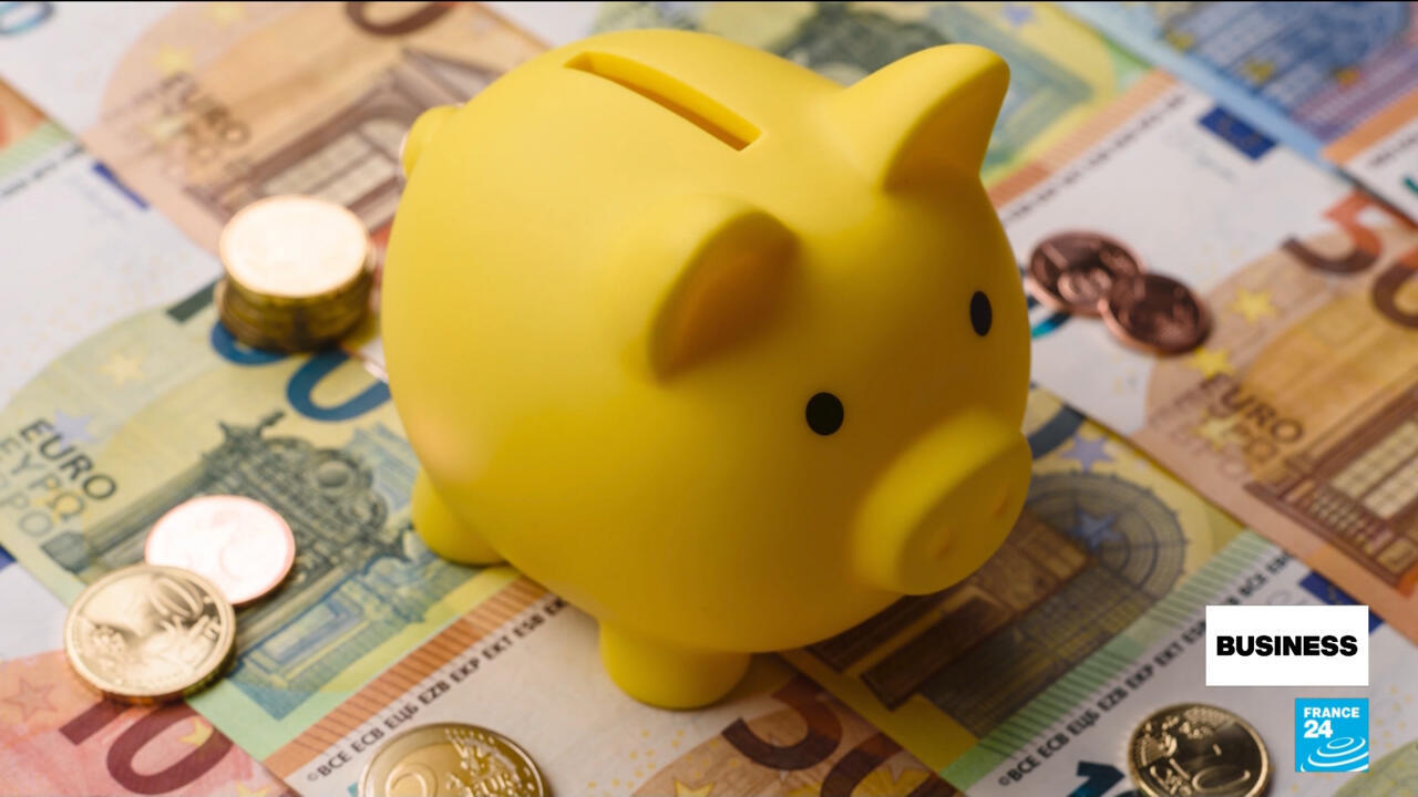 Yellow piggy bank sits on euro banknotes beside several euro coins.