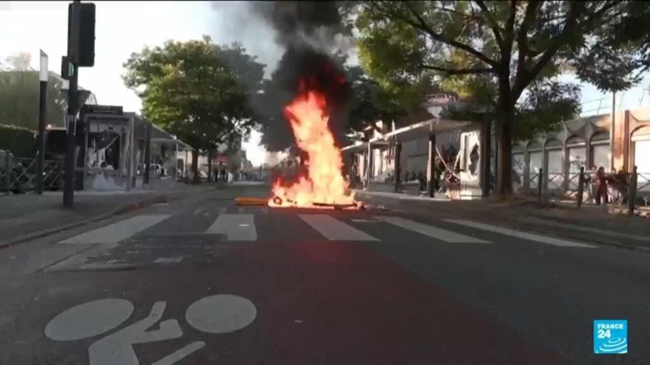 Flames and dark smoke rise from burning debris in the middle of a city street.