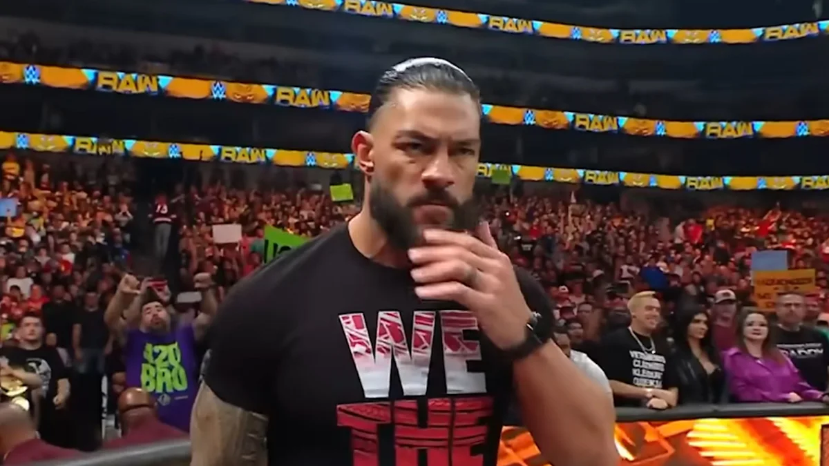 A bearded wrestler in a black WWE shirt stands near the ring with a hand at his chin.