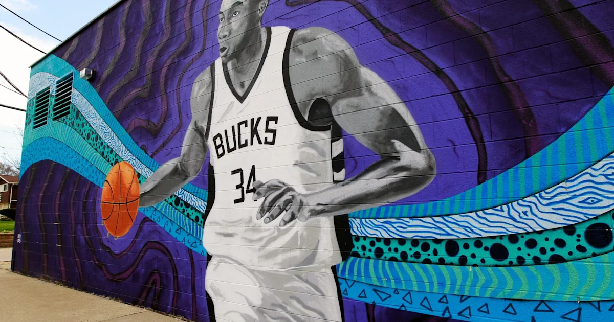 A mural depicts a basketball player in a Bucks number 34 jersey against a purple and turquoise background.