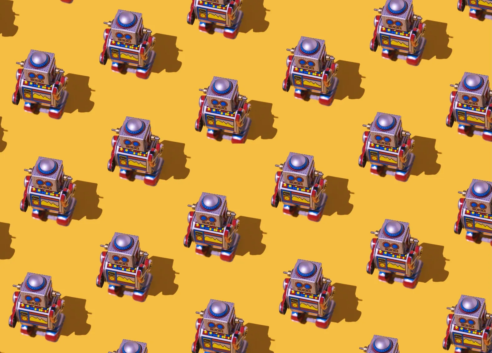 Rows of toy robots cast dark shadows across a bright yellow surface.