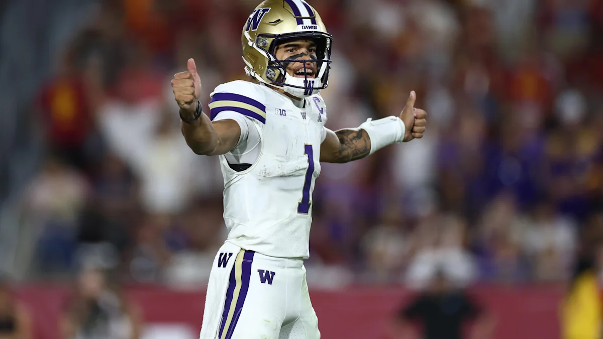 Washington player in a white uniform and gold helmet gives two thumbs up on the field.