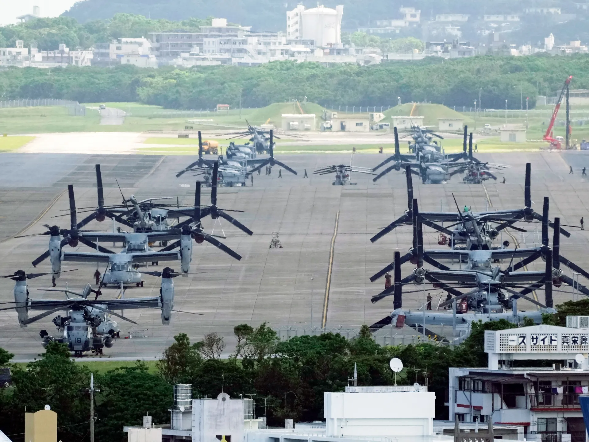 Military aircraft parked in rows on an airfield, with buildings and greenery beyond.