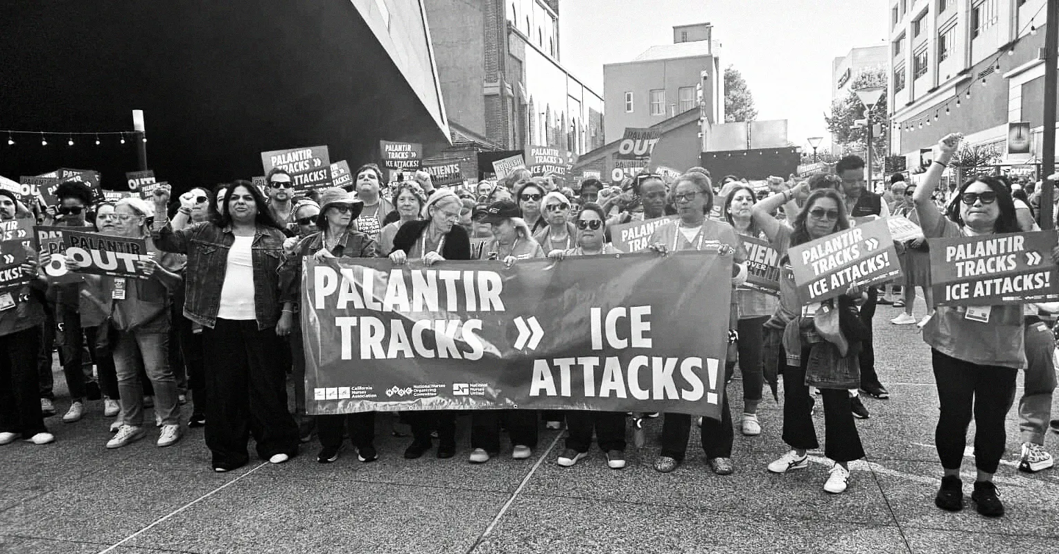 Black-and-white street protest with people holding a banner reading “Palantir tracks ICE attacks!”