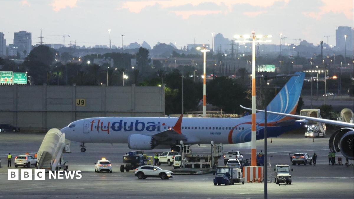Flydubai passenger plane parked on an airport apron at dusk, surrounded by service vehicles and ground staff.