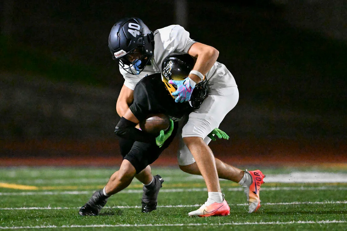 A white-uniformed football player tackles a ball carrier in black during a nighttime game.
