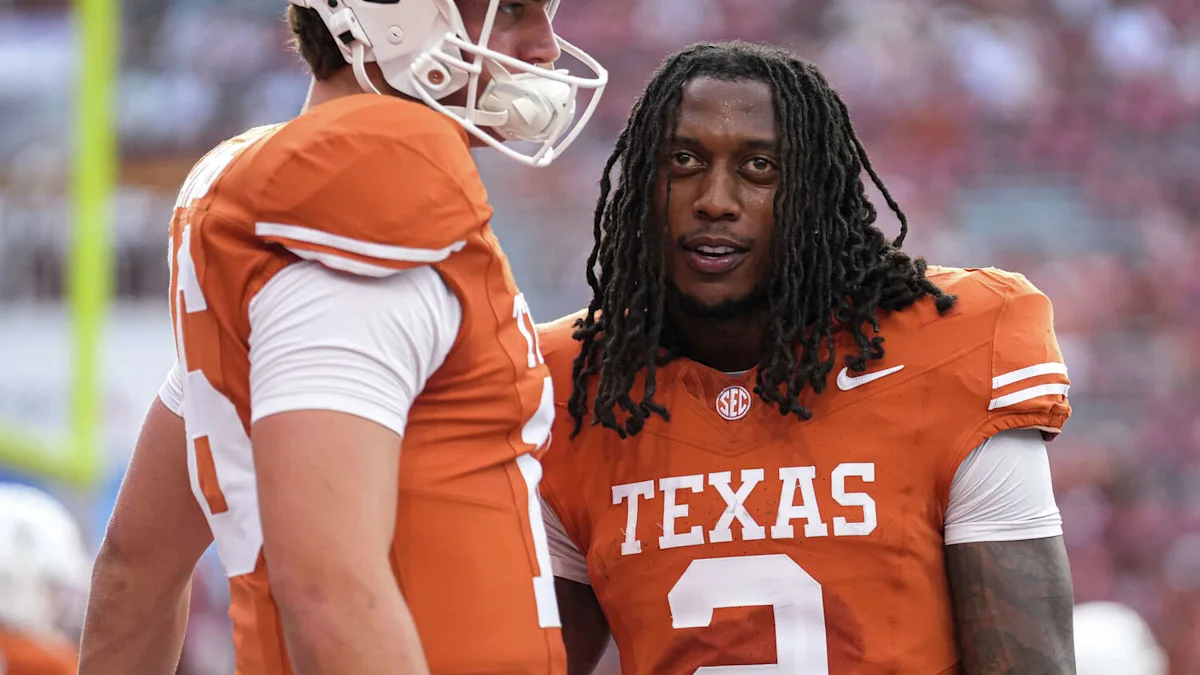 Texas player in orange jersey number 2 speaks with a helmeted teammate on the field.