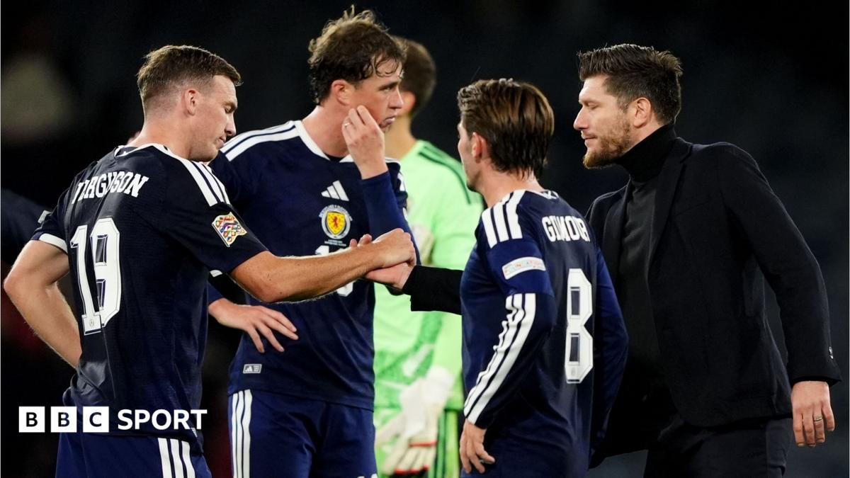 Three Scotland players in navy kits speak with a man in black on the pitch.