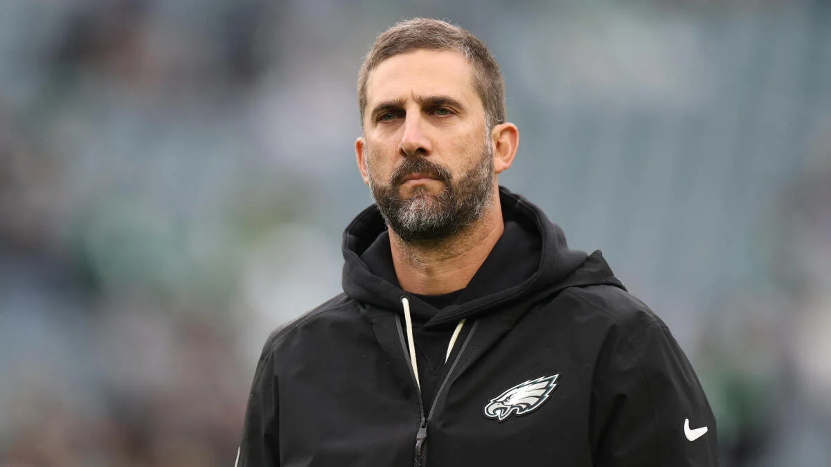 Bearded man in a black Eagles hoodie stands against a blurred stadium background.