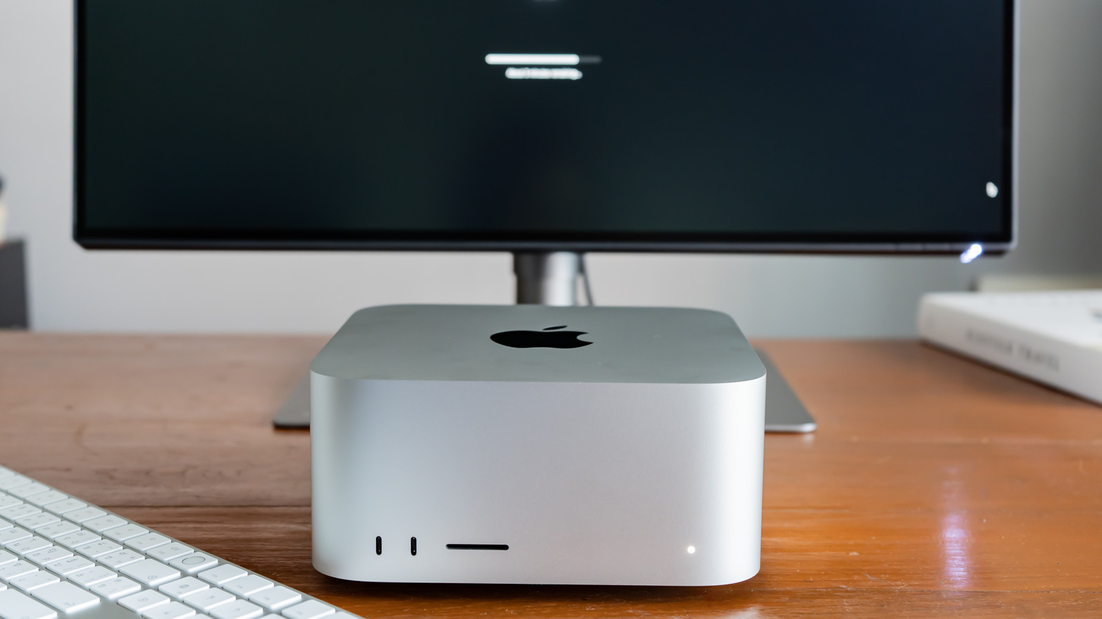 A silver Apple desktop computer sits on a wooden desk beneath a monitor, beside a white keyboard.