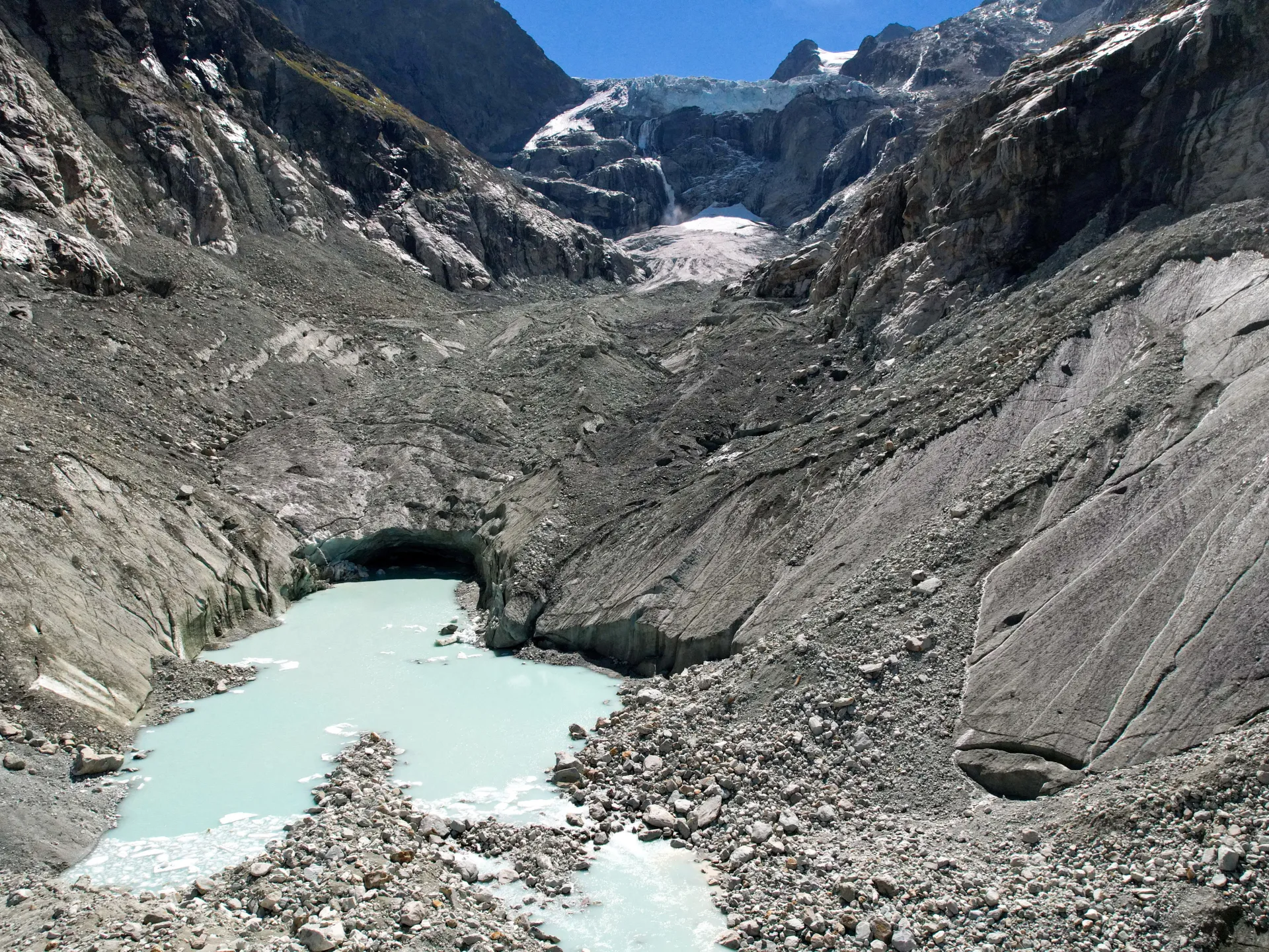 A milky turquoise pool below a rocky, mostly ice-free mountain basin, with a small glacier higher up.