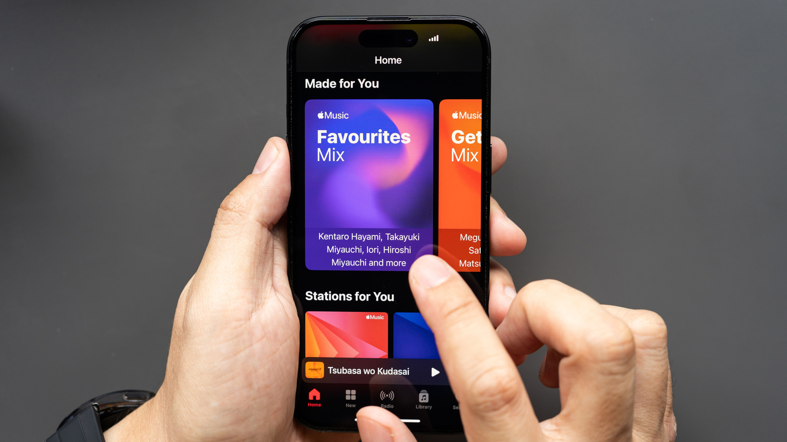 Hands hold an iPhone displaying Apple Music’s Home screen with personalized mixes and playback controls.
