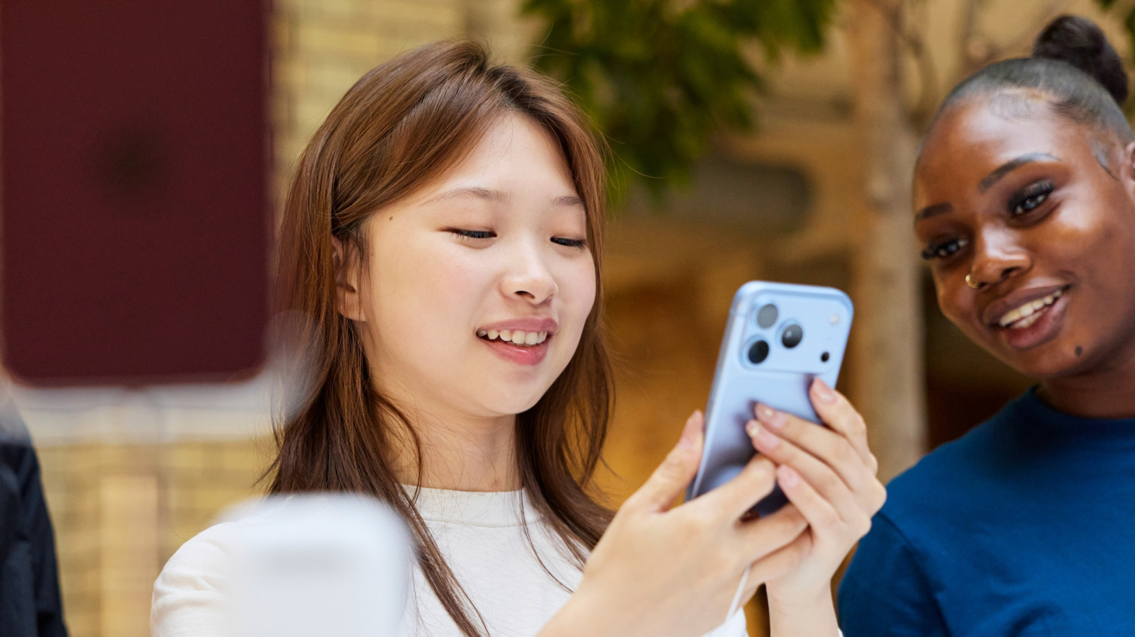 Two women smile while looking at a smartphone held by one of them.