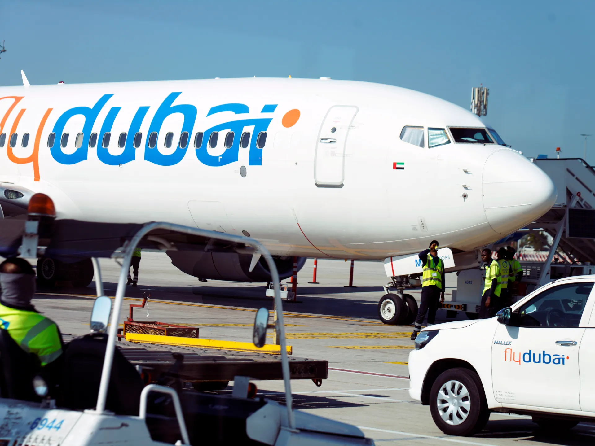 Flydubai passenger jet on an airport apron beside ground crew and a service vehicle.