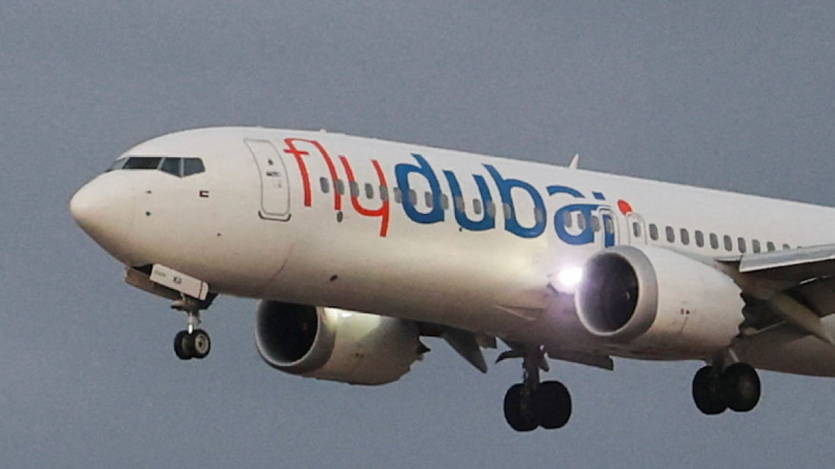 Flydubai passenger jet in flight with landing gear extended against a gray sky.