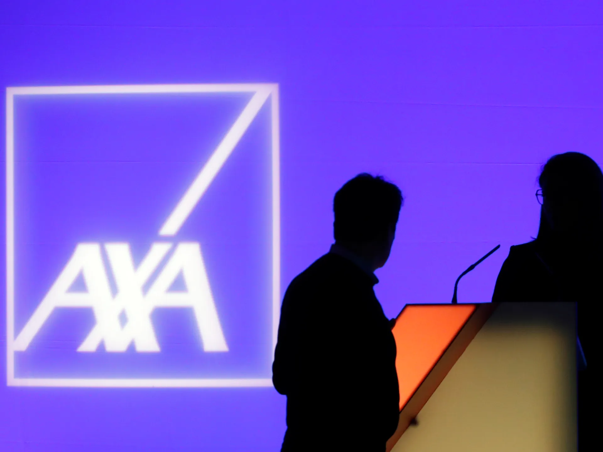Two silhouetted people stand beside a lectern against a purple backdrop displaying the AXA logo.