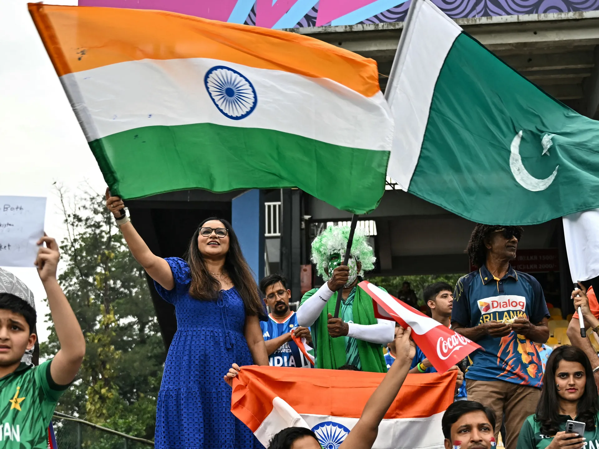 Crowd members wave Indian and Pakistani flags, with several wearing team jerseys and holding signs.