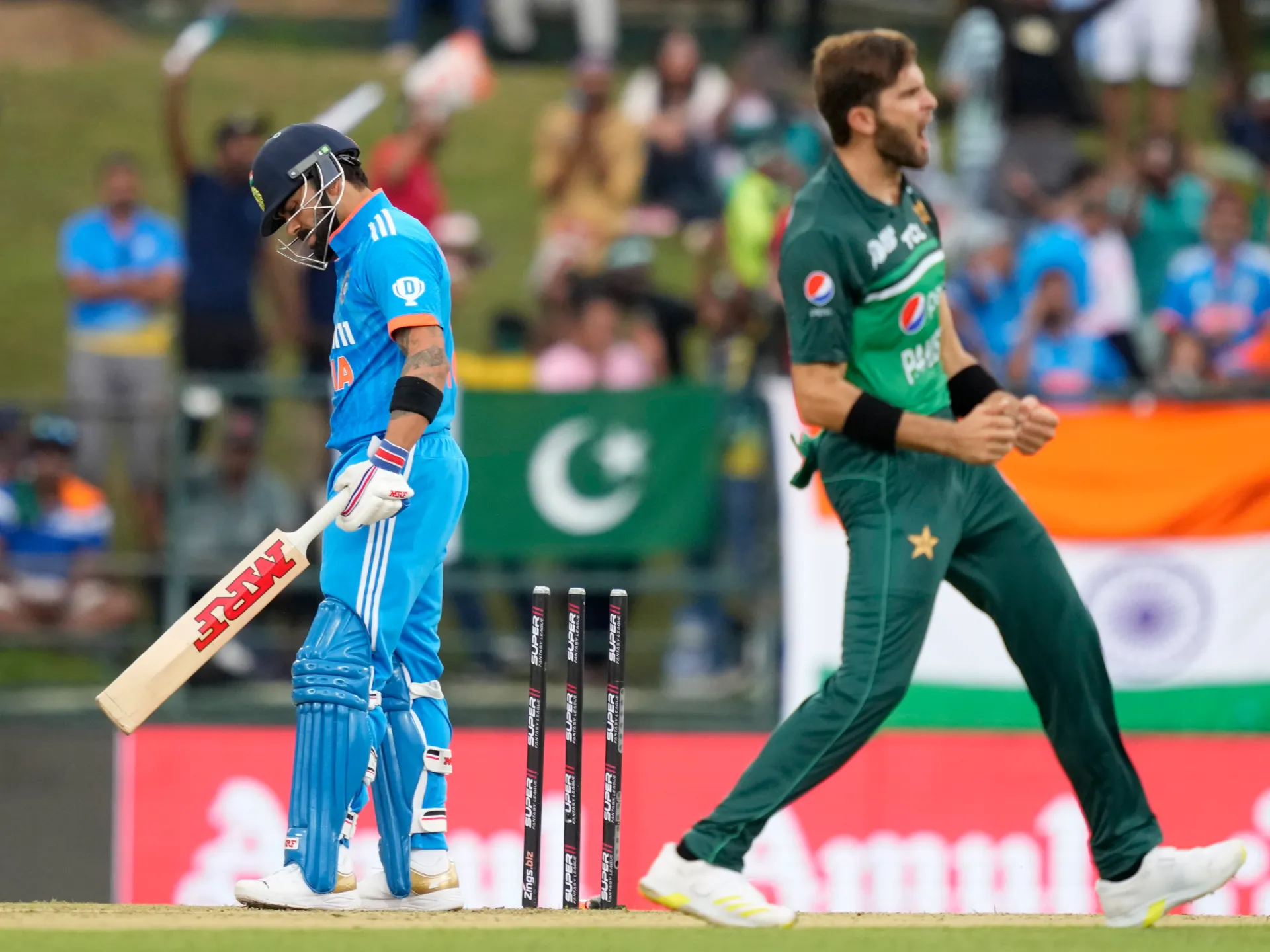 An Indian batter walks away as a Pakistan bowler celebrates beside the stumps during a cricket match.