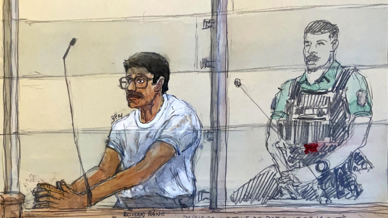Courtroom sketch shows a seated man in a white shirt beside an armed uniformed guard.