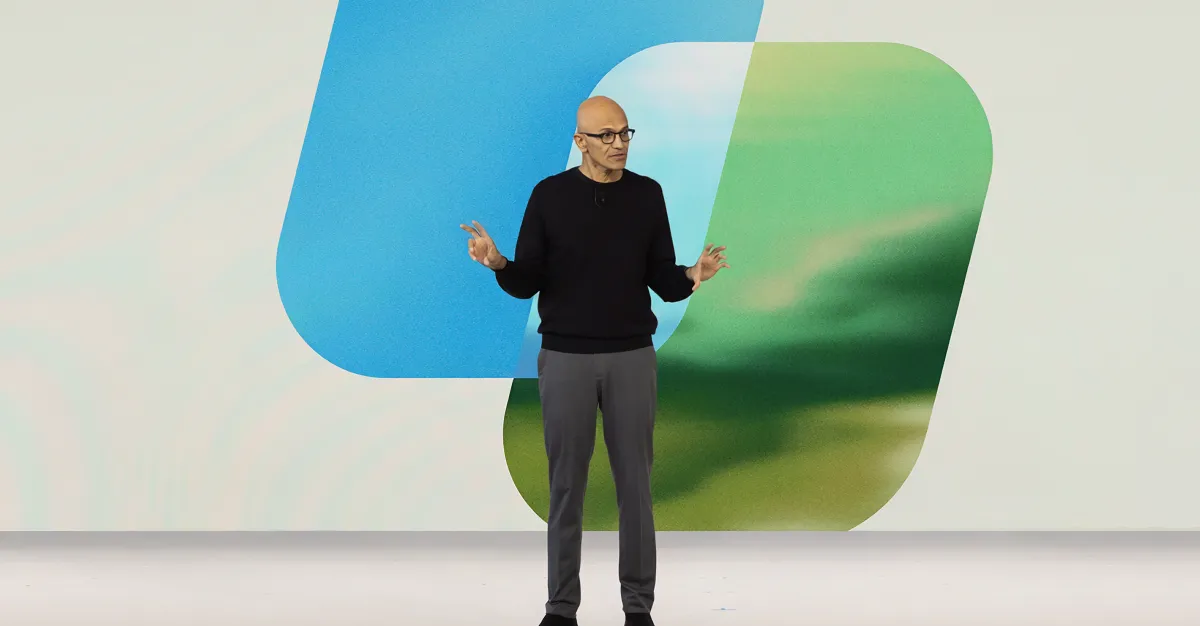 A bald man wearing glasses stands onstage before large blue and green abstract shapes.