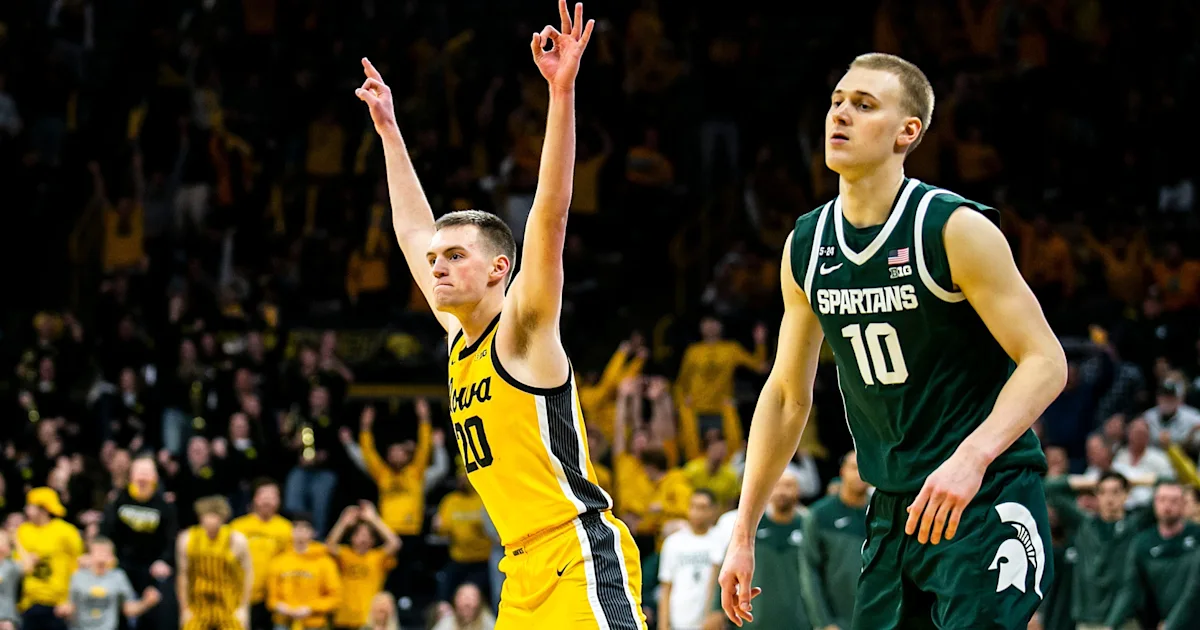 Iowa player raises both arms beside a Michigan State player during a basketball game.