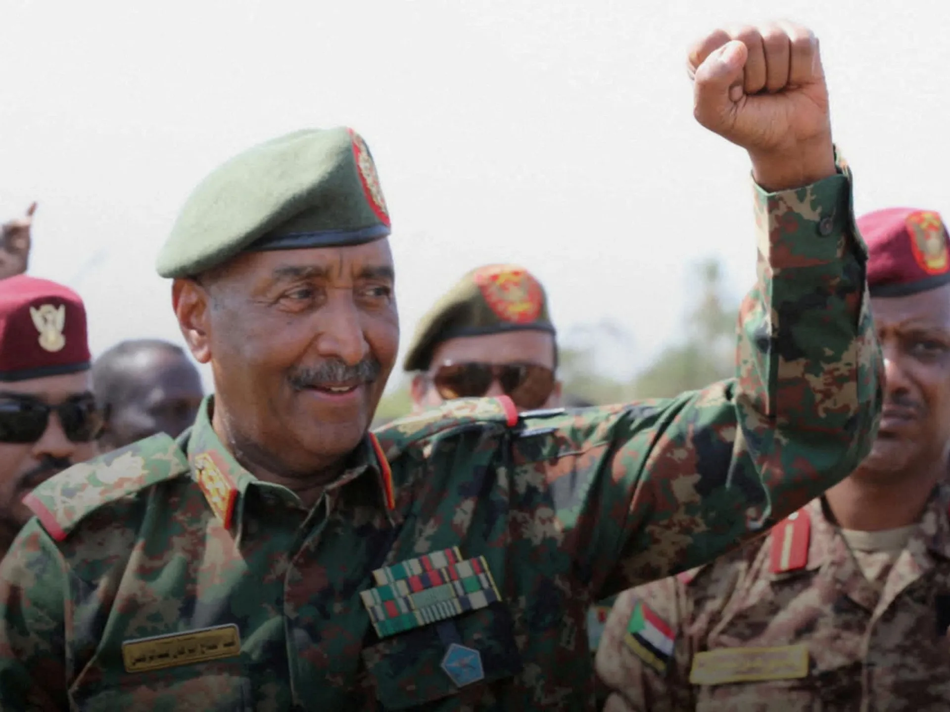 A uniformed officer raises a fist among soldiers wearing camouflage and berets.