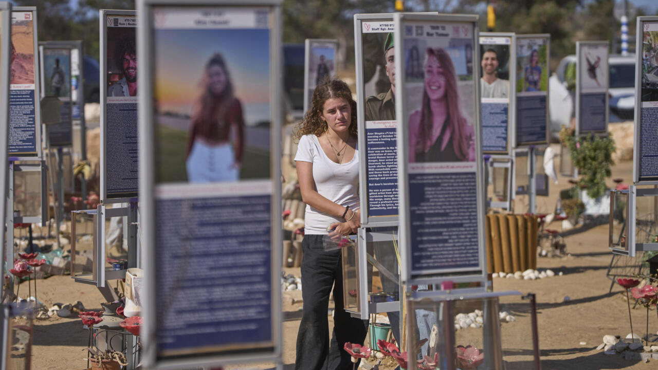 A woman stands among outdoor memorial displays featuring portraits, flowers, and stones.
