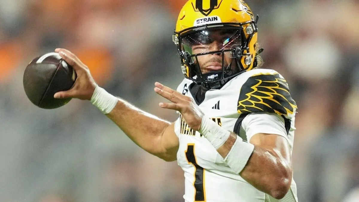 Football player in a yellow helmet and white jersey prepares to throw a ball.